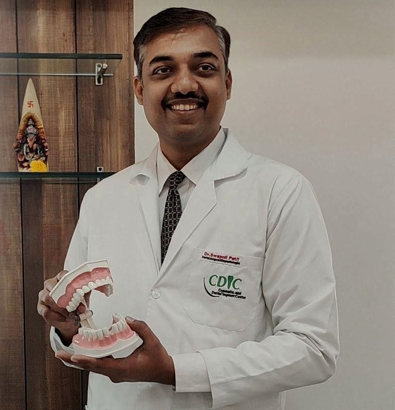 Dr. Swapnil B. Patil in a white coat, holding a model of the teeth and jaw.